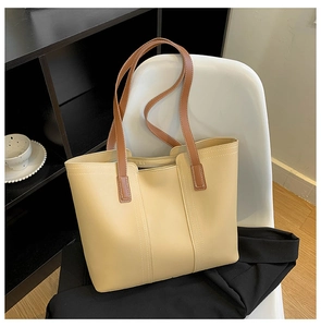 Close-up of a large beige tote bag with brown straps featuring decorative stitching details