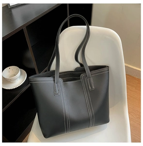 Detail of large black leather tote bag featuring contrast white double stitching on a chair