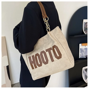 Dettaglio della borsa tote in tela beige con scritta HOOTO e maglia a catena dorata