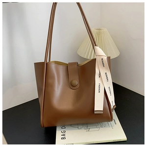 Détail d'un cabas en cuir marron mat avec sangle blanche 'FASHION' sur table noire