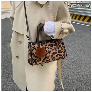 Outdoor street view of a leopard print faux fur handbag with leather straps and pompom
