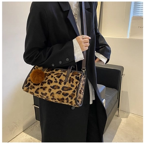 Detail view of a leopard print plush barrel bag with brown leather trim and pom-pom charm