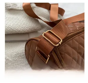 Gros plan sur la boucle dorée et la bandoulière large du sac cylindrique matelassé brun