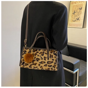 Detail shot of leopard print faux fur handbag featuring brown pompom and adjustable strap