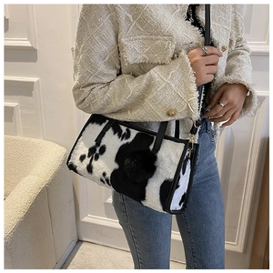 Detail of plush cow print handbag featuring black leather handles and faux fur pompom charm