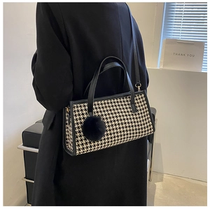 Detail of houndstooth plaid handbag featuring black faux fur pompom and leather trim