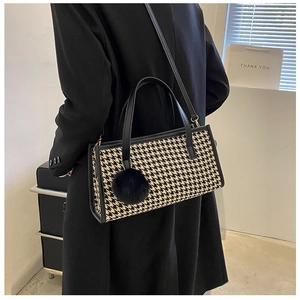 Detail of checkered pattern handbag with faux fur charm and leather strap on model