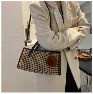 Close-up of houndstooth shoulder bag with plush ball charm on a model's outfit