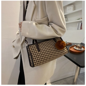 Detail of checkered plaid handbag with brown leather straps and plush pompom charm