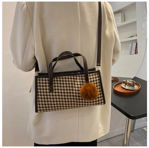 Houndstooth tote bag detail featuring brown leather trim and a soft pompom charm accessory