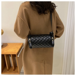 Détail d'un sac cylindrique matelassé noir avec finitions dorées porté par un mannequin