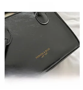Détail d'un sac en cuir verni noir avec logo doré et coutures texturées fines