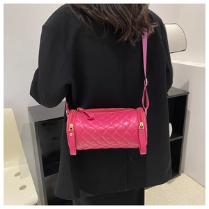 Détail du sac cylindre matelassé rose vif avec ferrures dorées sur un blazer noir
