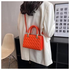 Rear view of a model wearing an orange quilted handbag with gold chain detail