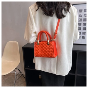 Model wearing a bright orange quilted crossbody bag with a unique braided handle detail