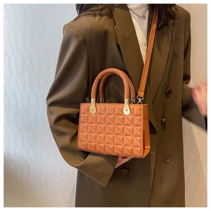 Close-up of brown geometric quilted PU leather handbag with woven handle and gold hardware