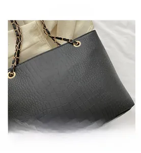 Detail of crocodile embossed leather texture and gold chain strap on black tote bag