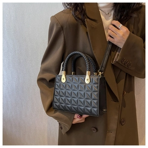 Detail of black quilted handbag with woven handle and gold hardware on model