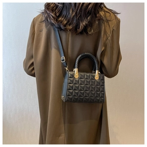 Detail of black quilted crossbody bag with woven handle and gold metal accents