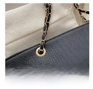 Close-up of crocodile texture handbag with gold grommet and metal chain strap
