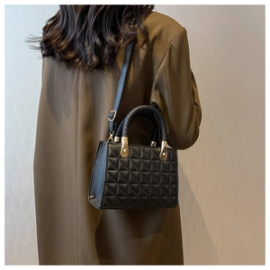 Detailed close-up of a black quilted handbag with woven handle and gold metal hardware