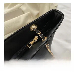 Detail of smooth gold zipper and crocodile texture on black leather shoulder bag