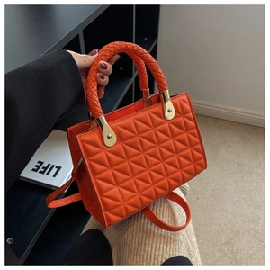 Detail of orange quilted crossbody bag with woven handles and gold metal hardware