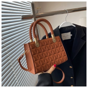 Close-up of brown quilted leather bag with woven cylindrical handle and gold metal hardware