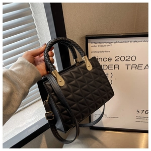 Detail of black quilted leather handbag with gold hardware and woven handle