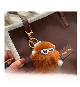 Détail d'un porte-clés monstre en peluche orange avec lunettes sur un sac fourre-tout