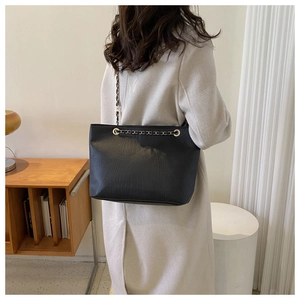 Close-up of black crocodile pattern tote bag with gold chain strap on model shoulder
