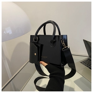 Détail du sac à main en cuir verni noir brillant avec lettrage doré et mini pochette