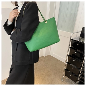 Detail of green crocodile embossed leather tote bag with gold chain strap on model