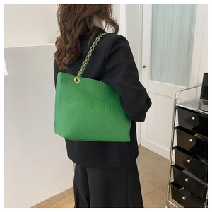 Detail view of green crocodile embossed tote bag with gold metal chain strap on model