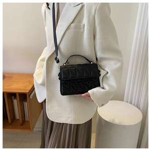 Detail of black quilted leather crossbody bag with chain trim and top handle held by model