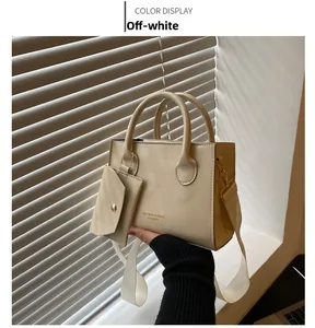Gros plan d'un cabas en cuir verni blanc crème avec lettrage doré et mini pochette