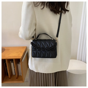 Detail of black quilted shoulder bag with decorative chunky chain and crossbody strap