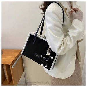 Détail d'un sac cabas noir avec bordure en molleton blanc et breloque en peluche tendance