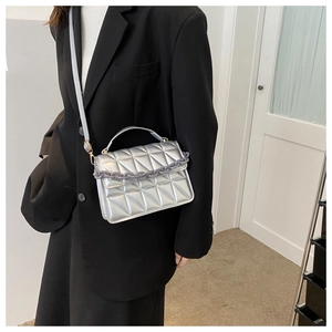 Close-up of a silver quilted handbag with chain detail worn by a model in a black suit