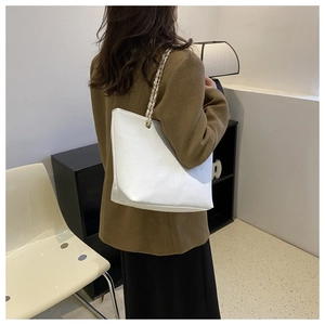 Detail of white crocodile-textured tote bag with elegant chain strap on shoulder