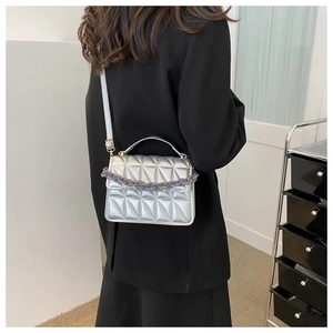 Detail of silver quilted crossbody bag with chunky grey chain strap on model outfit