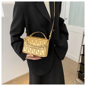 Detail of gold geometric quilted handbag with decorative chain and black blazer styling