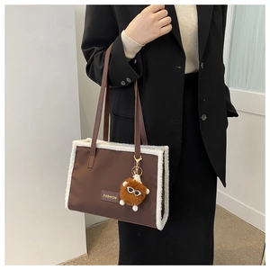 Détail d'un grand sac cabas marron avec bordure en peluche blanche et charme d'oeil
