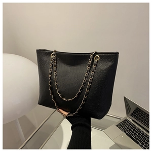 Detail of black croc-effect leather tote bag with elegant gold chain shoulder strap