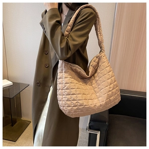 Detailed view of the beige quilted hobo bag texture and wide strap on an olive green coat