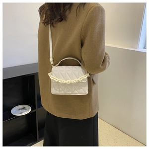 Detail view of a cream quilted crossbody bag featuring a thick decorative plastic chain