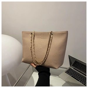 Detail of beige crocodile pattern tote bag featuring gold chain strap and textured finish