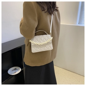 Close-up of cream quilted crossbody bag with chunky resin chain shown on shoulder