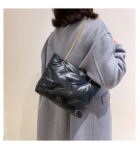 Detail einer schwarzen Stepptasche mit goldener Kette über einem grauen Wollmantel