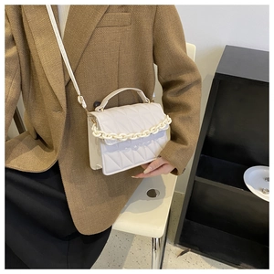Close-up of cream quilted crossbody bag featuring elegant chain detail and top handle